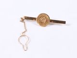 a gold tie bar with a coin attached to it