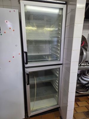 un réfrigérateur vide dans une cuisine où le plan de travail est encombré de nombreuses casseroles et poêles