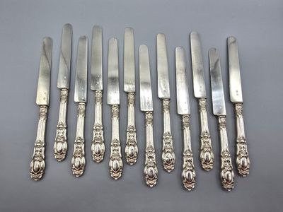 six couteaux argentés et six couteaux posés sur un support gris