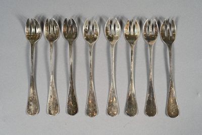 six cuillères et fourchettes en argent sont alignées sur une surface blanche
