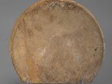 an old brown plate sitting on a metal stand on a gray surface
