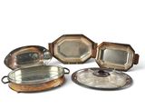 cinq plateaux en argent et une assiette en argent posés sur un plateau blanc