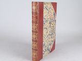 an old book with a red cover sitting on top of a white surface