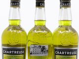 trois bouteilles de Chartreuse sont alignées sur une surface blanche