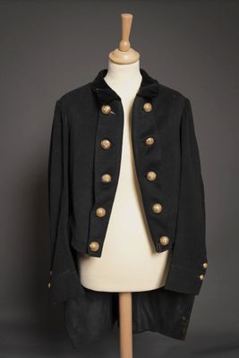 une veste noire à boutons dorés posée sur le torse d'un mannequin