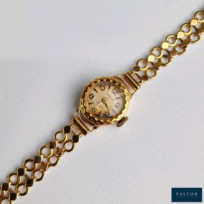 un gros plan d'une montre en or attachée à une chaîne, posée sur une surface blanche