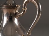 a silver coffee pot with a handle on a table