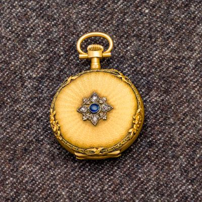 une image représentant une montre de poche en or ornée d'une pierre bleue au centre