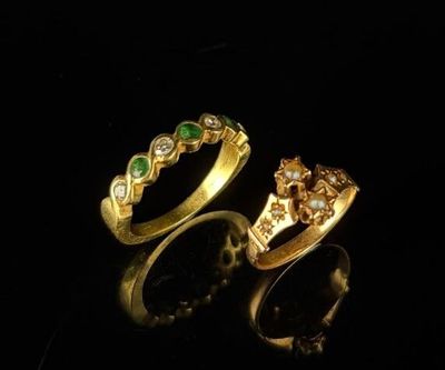 two gold rings with emeralds and diamonds on a black surface
