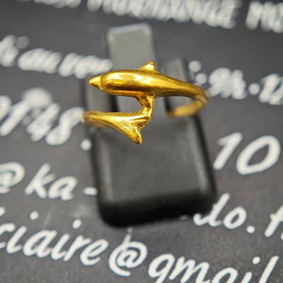 une bague en or ornée d'un dauphin, posée sur un téléphone portable