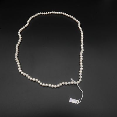 un collier de perles blanches muni d'un fermoir en argent, sur fond noir