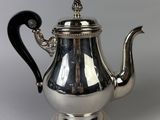 a silver teapot with a black handle on a white surface