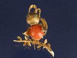 un oiseau doré orné d'une pierre rouge, perché sur une branche d'arbre
