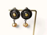 pair of black and gold earrings with pearls on a wooden stand