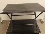 une table dont le plateau est noir, posée sur une palette en bois