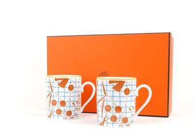 two coffee mugs in front of an orange box with a bird on it