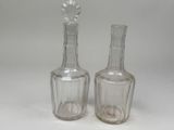 une paire de bouteilles en verre transparent posées sur une surface blanche, avec une fleur posée dessus