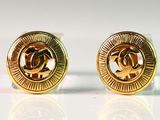 deux paires de boucles d'oreilles Chanel dorées posées sur une surface blanche