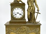 une horloge en or surmontée d'une statue représentant une femme tenant une épée