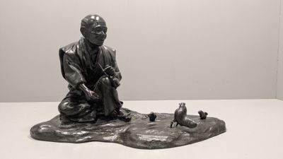 statue représentant un homme assis sur un rocher, avec des oiseaux devant lui