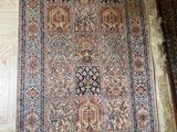 un grand tapis oriental posé sur un parquet, près d'un mur