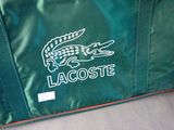 a green bag with a crocodile on it sitting on a bed