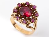 une image représentant une bague en or sertie d'une pierre rouge entourée de pierres violettes