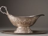 a silver gravy on a silver plate on a gray surface