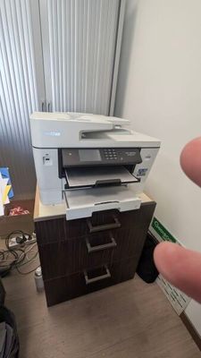 une main qui désigne une imprimante posée sur un bureau