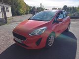 La voiture rouge est garée sur le parking, à côté d'une clôture.