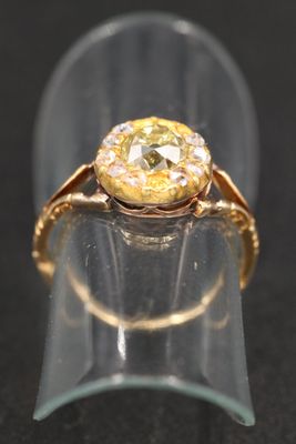 une image représentant une bague en or sertie d'un diamant jaune, posée sur un morceau de verre transparent