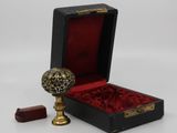 a small black box with a red velvet lining and a gold ball in it