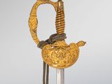a close up of a gold and silver sword on a wooden stand