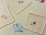 four napkins with embroidered flowers on them on a table