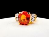 a close up of a ring with an orange stone surrounded by diamonds