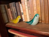 two birds sitting on a bookshelf next to some books