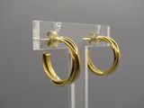un gros plan sur une paire de boucles d'oreilles créoles en or posées sur un présentoir transparent