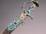 someone is holding a knife with a jeweled handle on a gray surface