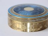 a gold box with a blue lid sitting on a white surface