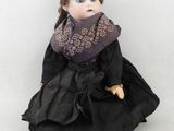 poupée assise par terre, vêtue d'une robe noire et d'un foulard