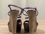 purple sued high heeled sandals on a wooden table with a curtain in the background