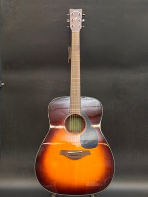 an acoustic guitar sitting on a stand in front of a black background