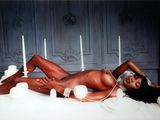 une femme nue allongée sur un lit, avec des bougies en arrière-plan