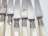 six knives with carved handles are lined up on a white surface