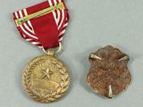 two medals with a red ribbon and a gold medal on a gray surface
