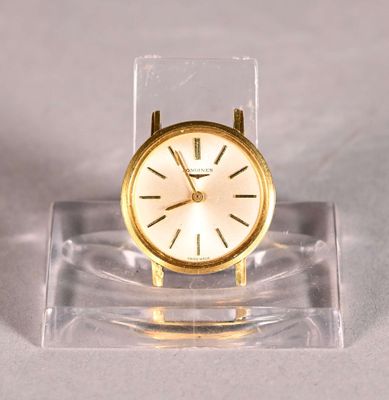 a small gold clock on a clear stand on a white surface