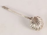 a silver spoon with a shell on it on a white surface