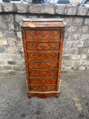 an antique chest of drawers on a sidewalk next to a stone wall