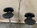 three black leather bar stools and a glass vase with a flower in it
