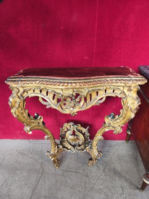 une console ancienne aux sculptures ouvragées, devant un mur rouge